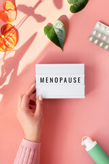 Text Menopause on light box in hand. HRT Replacement hormone therapy, HRT concept. Pink background...