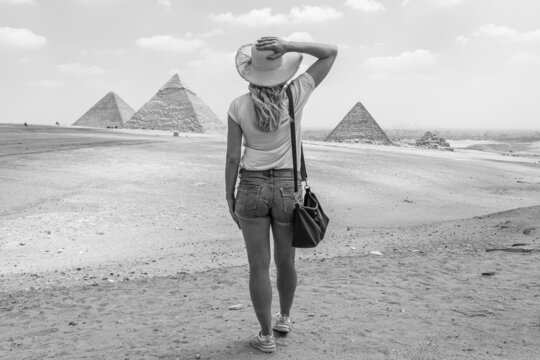 Young girl in the desert. Back view portrait of a single woman watching the Great Pyramids of Giza in Egypt. Black and White image.
