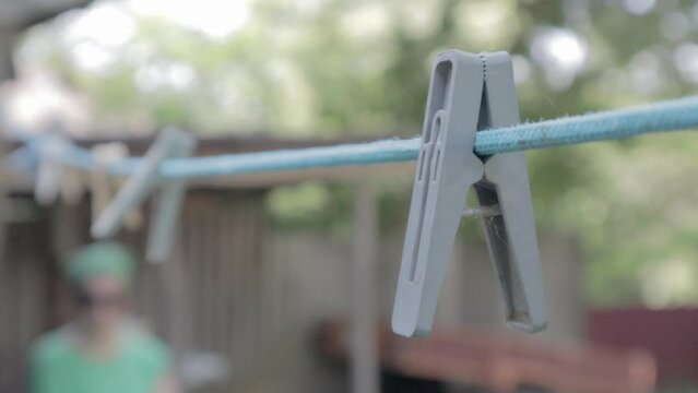Plastic clothespins hang in a row on the rope. Rope outdoors, on a blurred background in a sunny garden. Clothesline on the street. Clothespins.