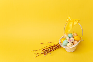 Easter eggs in basket and willow branches on the yellow background. Easter postcard. Copy space for text
