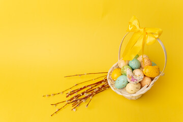 Easter eggs in basket and willow branches on the yellow background. Easter postcard. Copy space for text