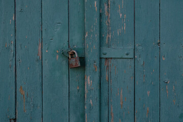 Vintage blue wooden painted door of old building. Shabby door boards. Old peeling painted door, crumbles. Rusty metal lock on the door. Threadbare Wooden rustic background. 