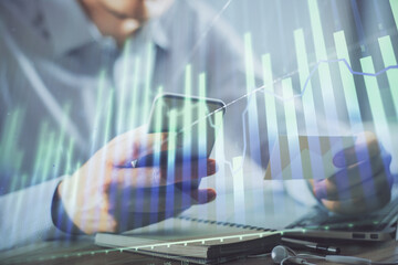 Double exposure of man's hands holding and using a phone and financial graph drawing. Analysis concept.