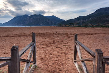 Fototapeta premium Fence and gate on a sandy beach against the backdrop of mountains at dawn.