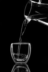 water pours into a glass from a decanter on black background
