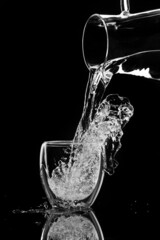 water pours into a glass from a decanter on black background