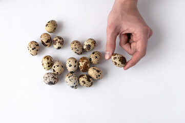 man's hand holds a quail egg on a white background. Top view of group of eggs. The concept of healthy breakfast. Home cooking