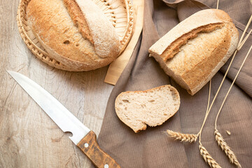 loaf of fresh bread and cutted slice of baguette on wooden background with knife and copy space,...