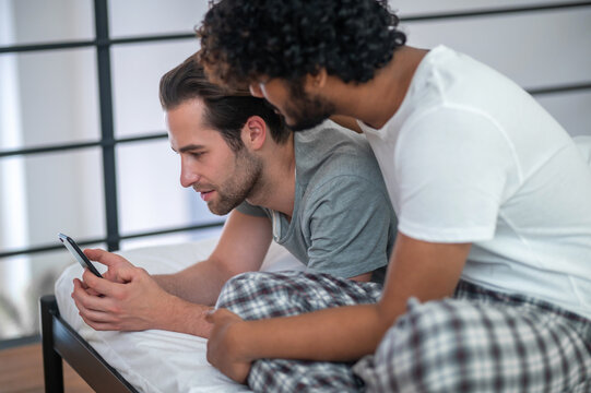Biracial gay couple staring at the smartphone screen
