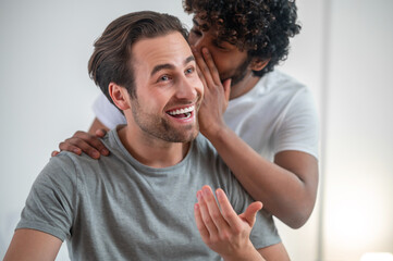 Indian man telling a secret to his pleased Caucasian boyfriend