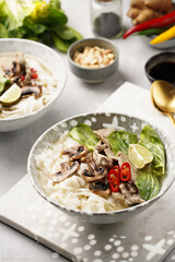Pho Bo vietnamese soup with beef, rice noodles, pak choi and mushrooms in a grey bowl on marble board, peanuts, soy sauce, chilli