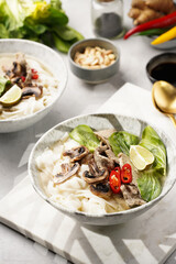 Pho Bo vietnamese soup with beef, rice noodles, pak choi and mushrooms in a grey bowl on marble board, peanuts, soy sauce, chilli