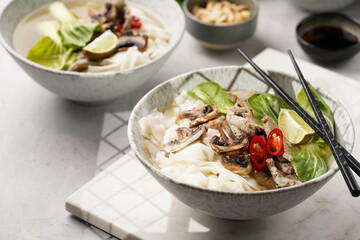 Pho Bo vietnamese soup with beef, rice noodles, pak choi and mushrooms in a grey bowl on marble board, peanuts, soy sauce, chilli