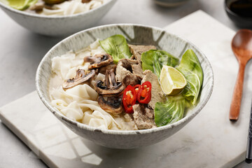 Pho Bo vietnamese soup with beef, rice noodles, pak choi and mushrooms in a grey bowl on marble board, peanuts, soy sauce, chilli