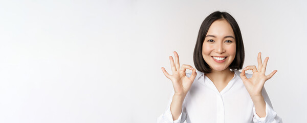 Close up head portrait of asian girl showing okay, ok sign and smiling satisfied, recommending,...