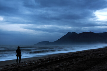 Silhouette of a man on the shores of the Mediterranean Sea, against the backdrop of mountains, at night, sea, mountains, man, night.