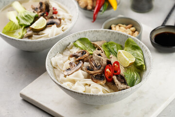 Pho Bo vietnamese soup with beef, rice noodles, pak choi and mushrooms in a grey bowl on marble board, peanuts, soy sauce, chilli