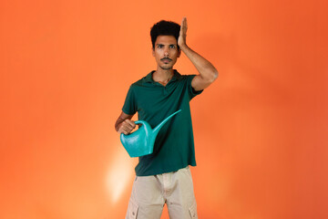 Earth Day - Handsome young black man with green watering can holding plant isolated on orange background.