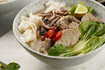 Pho Bo vietnamese soup with beef, rice noodles, pak choi and mushrooms in a grey bowl on marble...