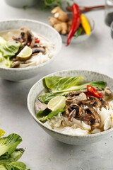 Pho Bo vietnamese soup with beef, rice noodles, pak choi and mushrooms in a grey bowl, peanuts, soy sauce, chilli