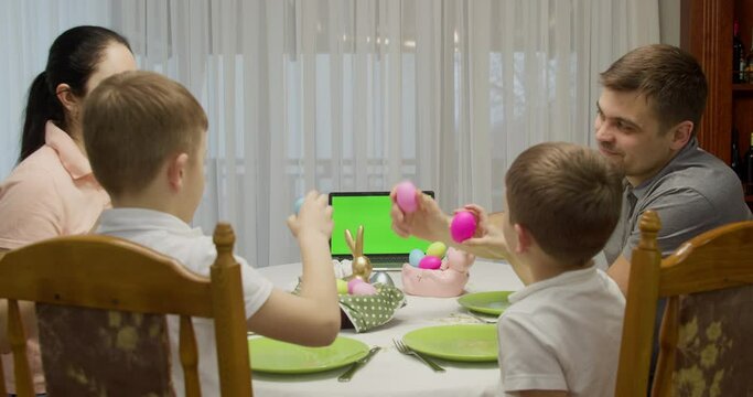 Family of four talking and having dinner, sitting at the table. on the table is a computer with a green screen