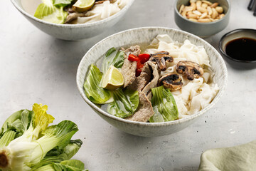 Pho Bo vietnamese soup with beef, rice noodles, pak choi and mushrooms in a grey bowl, peanuts, soy...