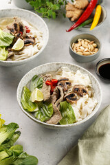Pho Bo vietnamese soup with beef, rice noodles, pak choi and mushrooms in a grey bowl, peanuts, soy sauce, chilli