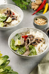 Pho Bo vietnamese soup with beef, rice noodles, pak choi and mushrooms in a grey bowl, peanuts, soy sauce, chilli