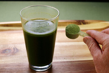 Hand Showing a Scoop of Organic Celery Powder Near Beverage