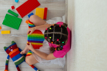 little brunette girl in bright colorful clothes, sits at home, on the floor