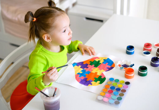The child looks forward in surprise with bulging eyes. Profile of a astonished girl drawing a postcard for Autism Day with a picture of puzzles