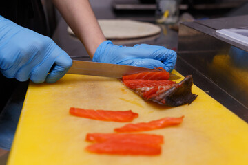 The hands of the cook in hygienic gloves with a sharp knife separate the salmon fillets from the...
