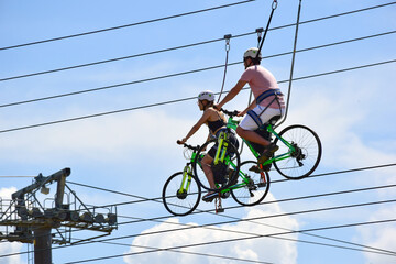 At the attraction, a guy and a girl ride on bicycles on hanging ropes and smile. Against the background of the blue sky.