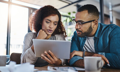 Searching for an insurance policy that suits their needs. Shot of a young couple using a digital tablet while planning their budget together at home.