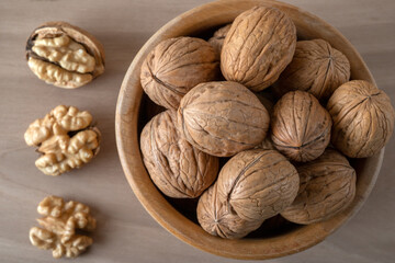 Walnut kernels and whole walnuts in bowl on wooden background