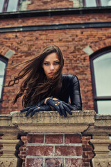 Giving you a piercing gaze. Seductive young woman in a black catsuit looking at you from a rooftop.
