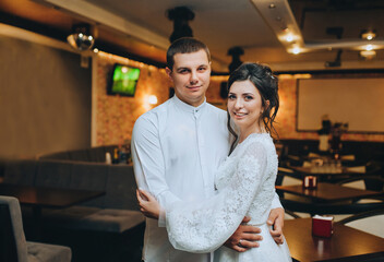 Beautiful, young bride and groom are hugging in the room, interior. Wedding portrait of stylish groom and cute bride in white lace dress.