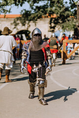 A strong knight, a warrior stands walking across the battlefield, guarding the state in armor with an ax in his hand in the Middle Ages.