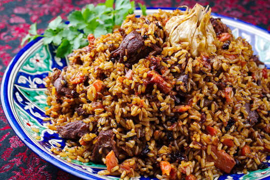Traditionelles usbekisches Fergana Plov mit Devsira Reis und Lammfleisch serviert als close-up auf einer handgefertigten bemalten Lagan Platte