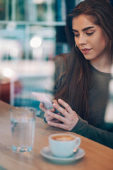 Woman using smartphone and drinking coffee in a cafe.