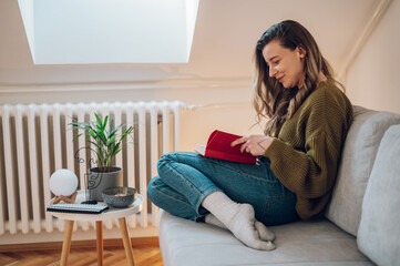 Obraz premium Woman reading a book while sitting on the couch at home