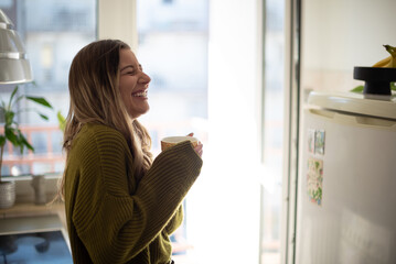 Woman standing in the kitchen and drinking cup of tea