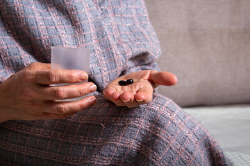Obraz premium Old woman holding in hand black pills.