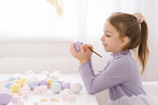 little girl child with hearing aids paints an easter egg with brush, children's easter creativity handmade
