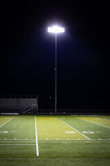 Fototapeta na wymiar Stadium lights on a poll next to American football high school field with artificial grass surface
