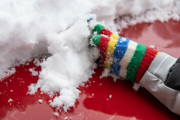 Kid s hand in a stripes glove retiring snow from a red van.