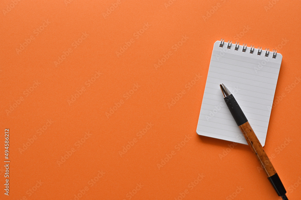 Poster a notebook and pen in a simple composition on orange background. copy space available.
