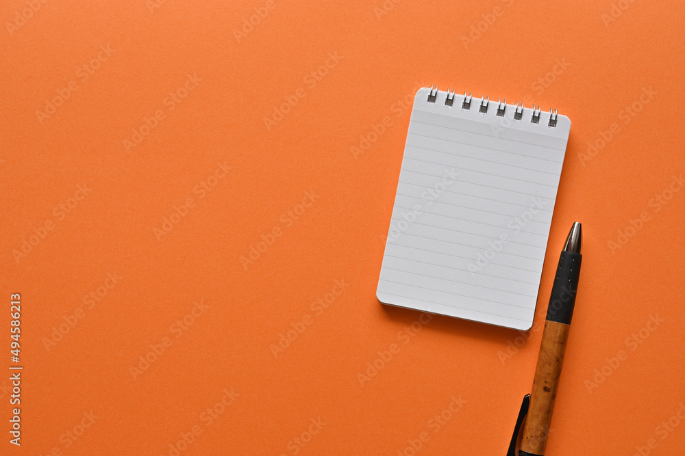 Poster a notebook and pen in a simple composition on orange background. copy space available.