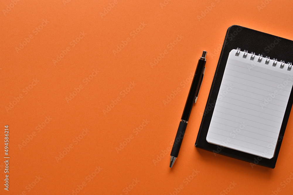 Poster a notebook and pen in a simple composition on orange background. copy space available.
