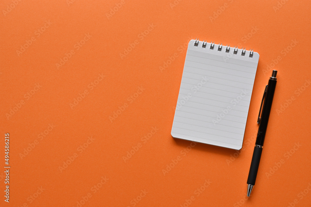 Poster a notebook and pen in a simple composition on orange background. copy space available.